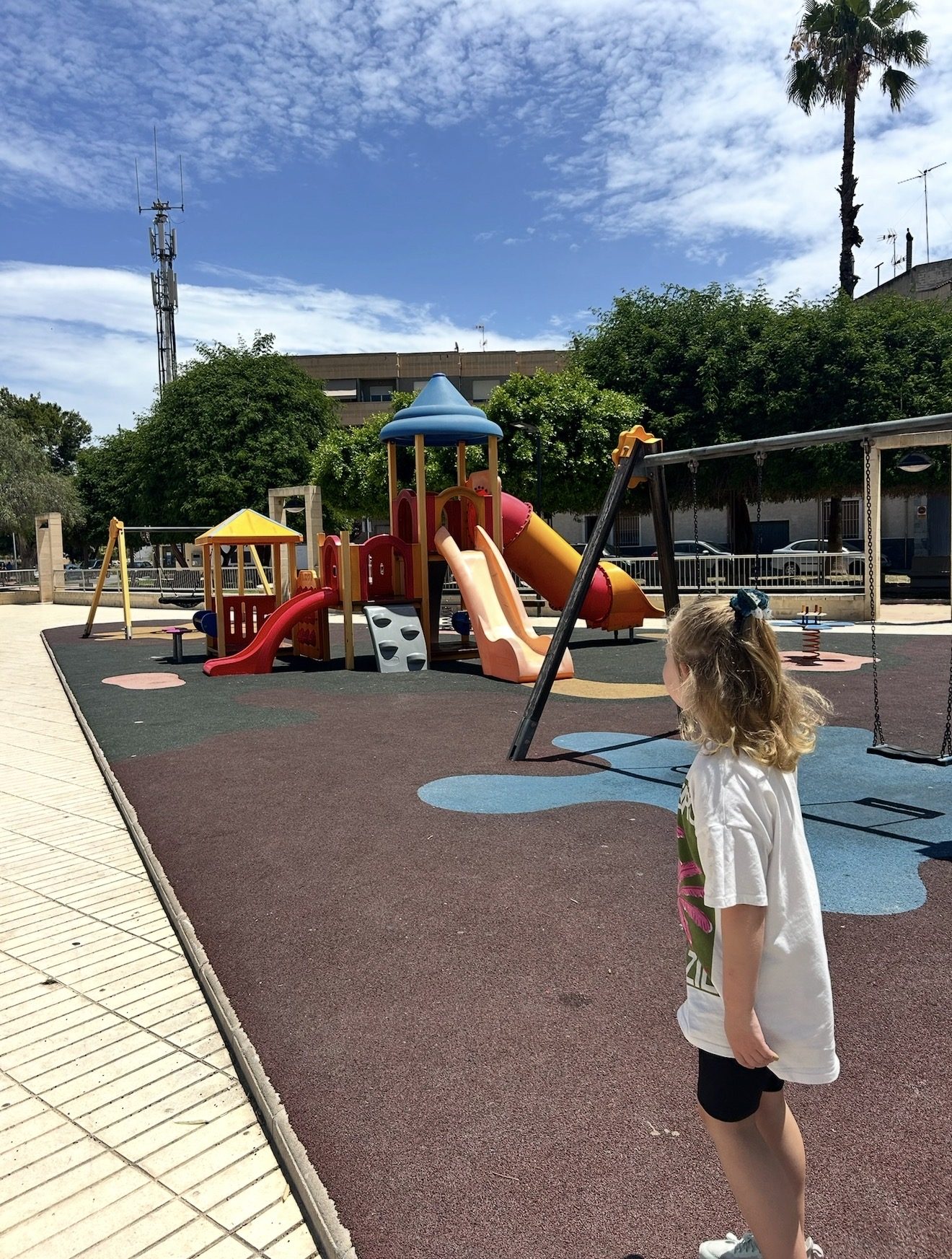 Our daughter beside a colourful Spanish town-square playground with slides and swings
