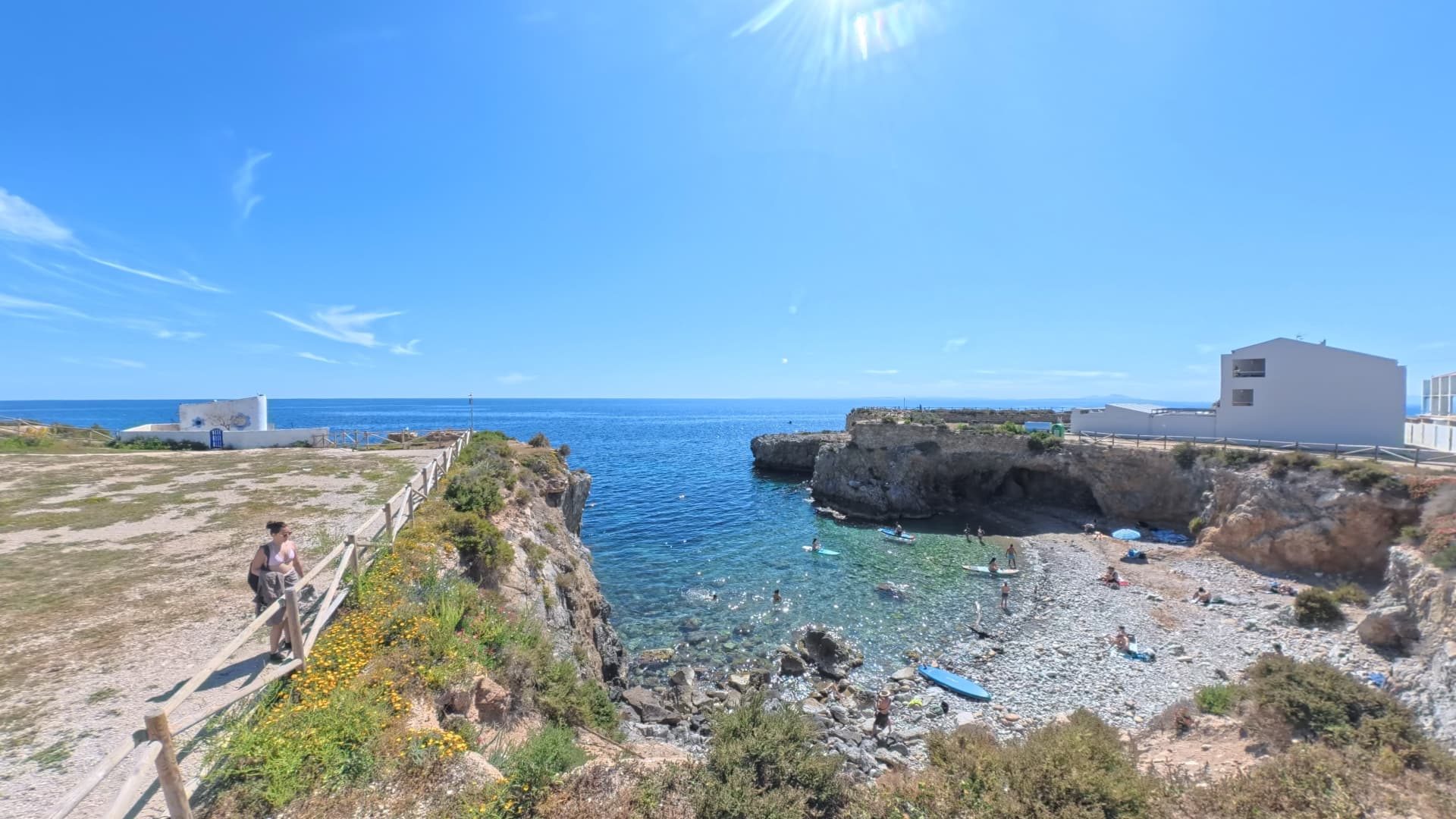 A clifftop path above a clear rocky cove with paddleboarders on the Orihuela Costa